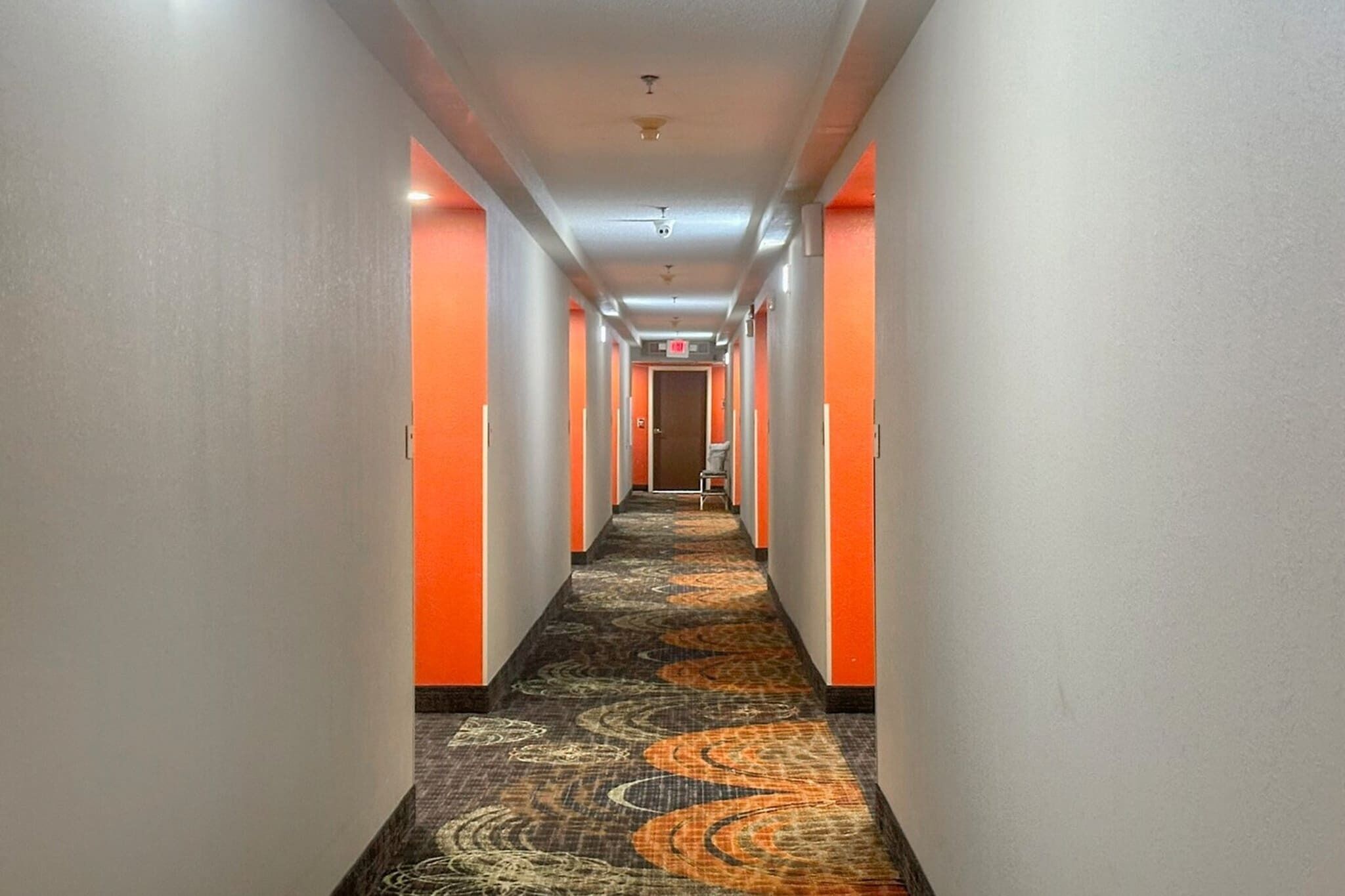 A hotel hallway with a carpeted floor, orange walls, and a door at the end.