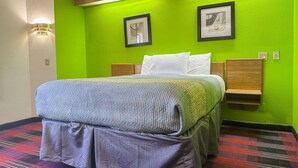 Een hotelkamer met een bed, groene wanden, twee ingelijste foto's, een nachtkastje en een wandlamp.