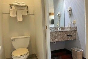 Un baño con inodoro, un perchero con toallas dobladas, un secador de pelo y un cubo de basura.