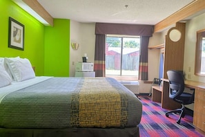 A hotel room with a bed, desk, chair, and a view of the outside.