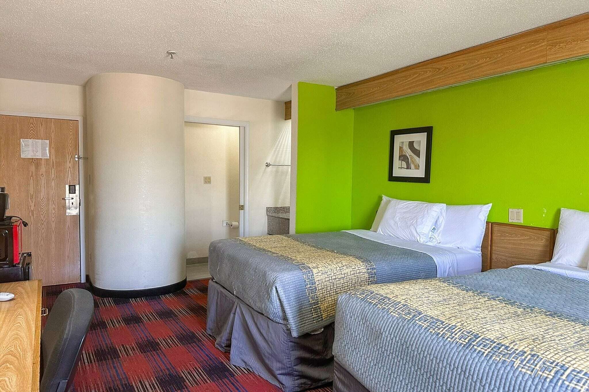 Habitació d'hotel amb dos llits, una porta de fusta, una paret decorativa verda i un quadre amb marc.