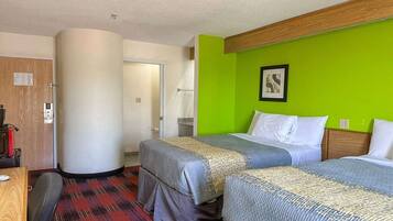 Habitació d'hotel amb dos llits, una porta de fusta, una paret decorativa verda i un quadre amb marc.