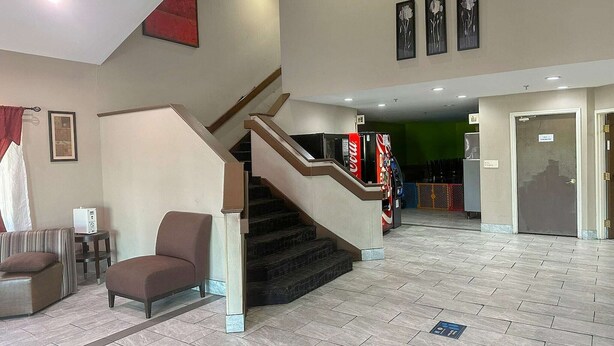 Vestíbulo de hotel con escalera, zona de estar y mostrador de recepción.