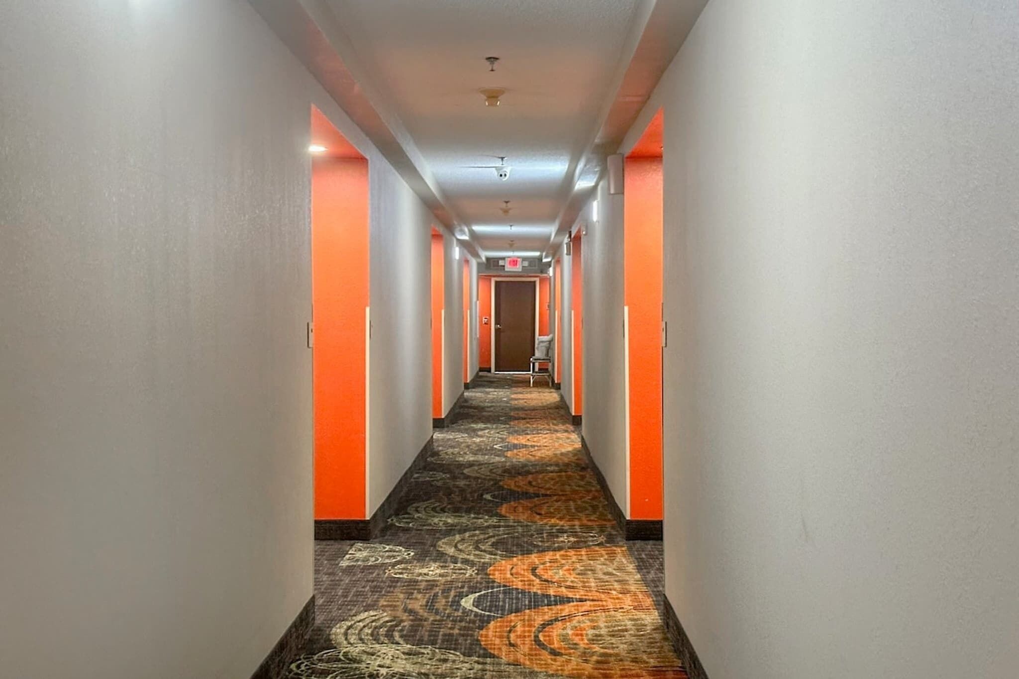 Un couloir d’hôtel avec un sol recouvert de moquette, des murs orange et une porte au bout.