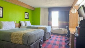 Een hotelkamer met twee bedden, een bureau met een computer, een televisie en een raam met gordijnen.