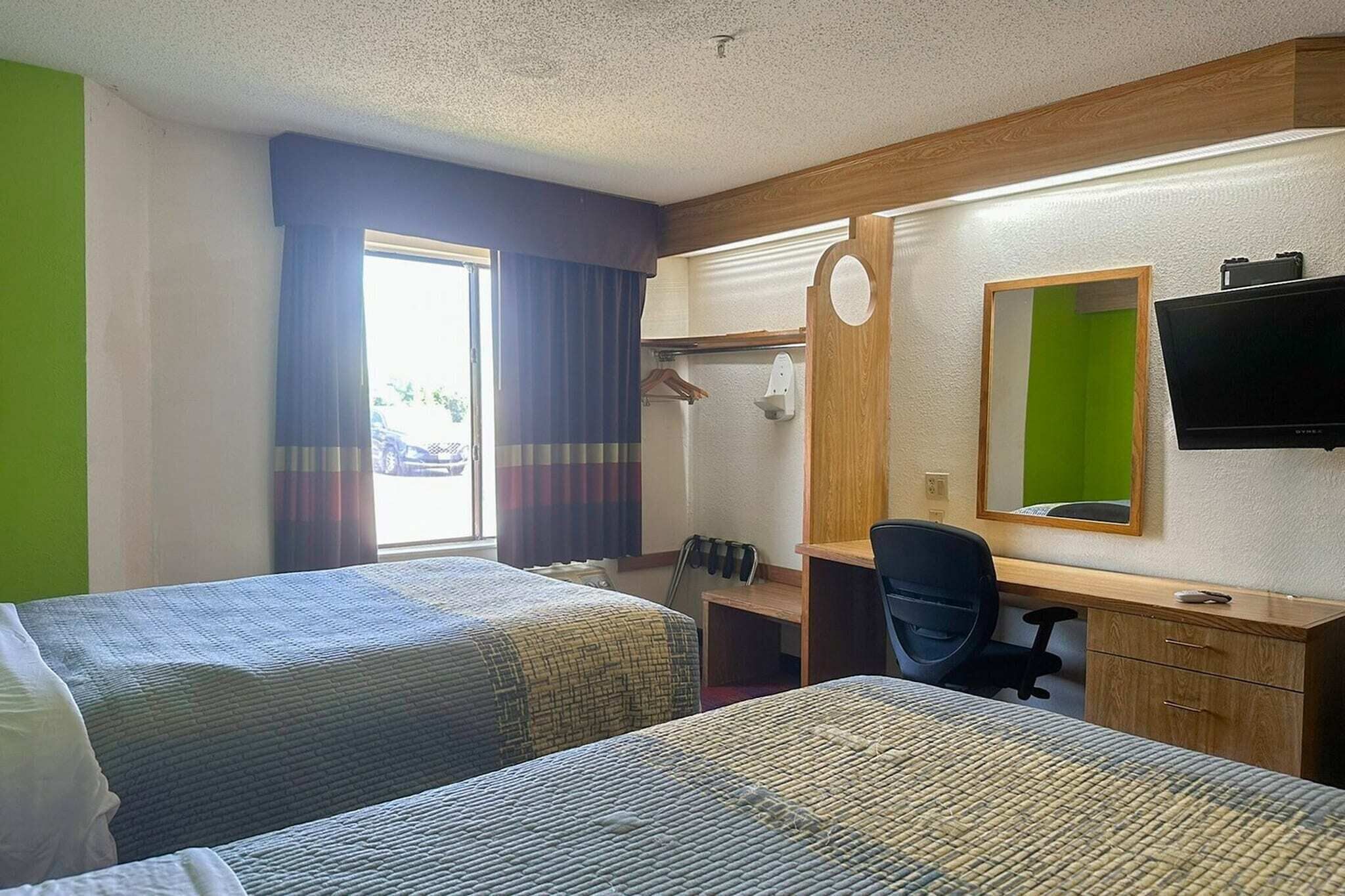 A hotel room with two beds, a desk, a chair, a TV, and a mirror.