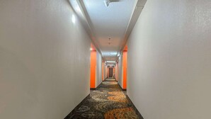 Een hotelgang met een kamerbreed tapijt, witte muren en oranje accenten.