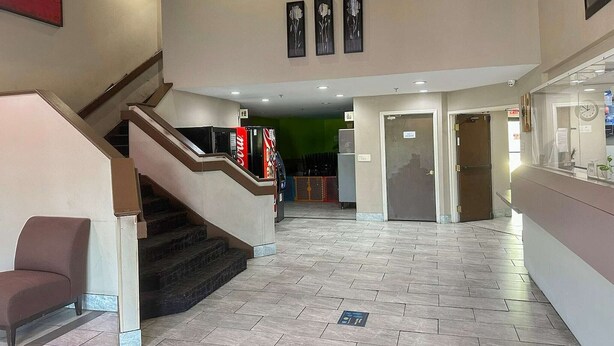 Een hotel lobby met een trap, een receptiebalie en een groene wand op de achtergrond.
