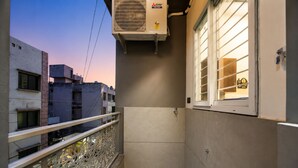 Ein schmaler Balkon mit schmiedeeisernem Geländer, ein Fenster mit Jalousien und eine Wand-Klimaanlage.