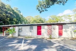 Un bâtiment d’un seul étage avec une porte rouge, un petit espace couvert doté d’un toit rouge et un parking à l’avant.