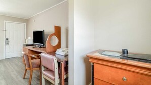 Habitación de hotel con un escritorio de madera, una silla, un televisor, una mesita y una puerta blanca.