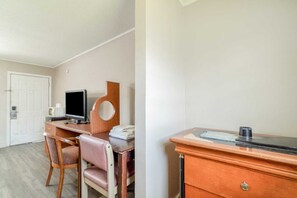 A hotel room with a wooden desk, a chair, a television, a small table, and a white door.