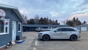 Un quartier résidentiel où un VUS blanc est garé devant un immeuble sur lequel est fixé un panier de basketball.