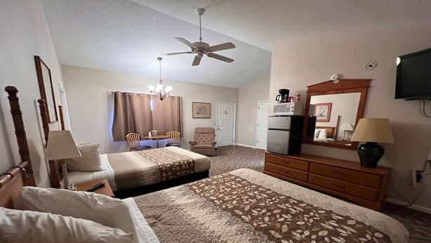 Une chambre d’hôtel avec deux lits, un ventilateur de plafond, une télévision, une commode et un coin repas avec des chaises et une table.
