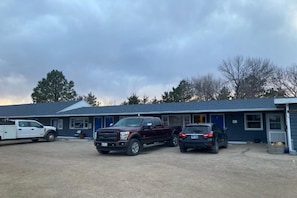 A building with a blue exterior, a gravel parking area, and three vehicles parked in front.