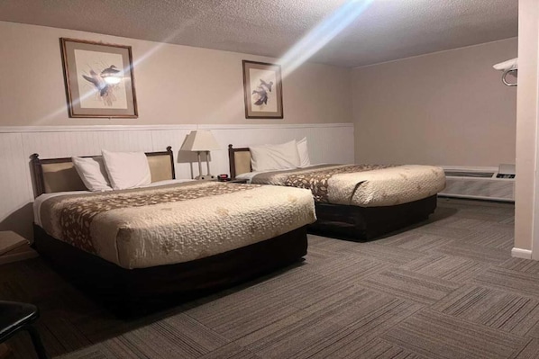 Quarto de hotel com duas camas, mesa de cabeceira, luminária e quadros nas paredes.