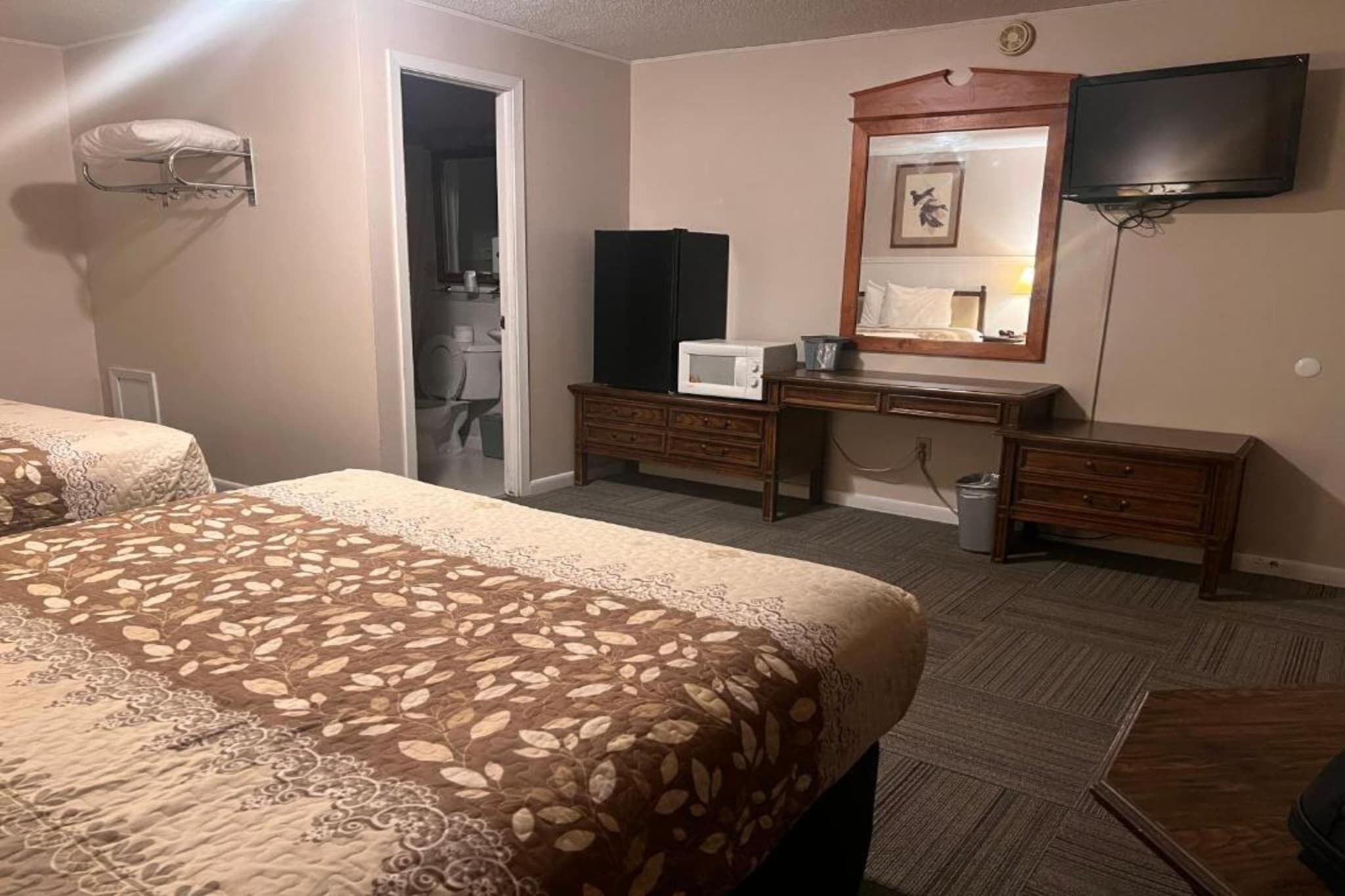 A hotel room with a bed, a desk with a mirror, a television, and a microwave.