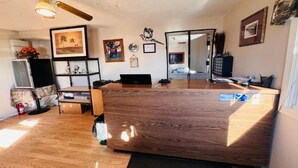 A spacious room with a wooden floor, a ceiling fan, a desk, a chair, a bookshelf, and a door leading to another room. - Suite 2 Queen Beds|Non-Smoking (Miller SD)