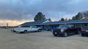 A building with a blue roof, a white utility truck, and a maroon pickup truck parked in front. - Suite 2 Queen Beds|Non-Smoking (Miller SD)