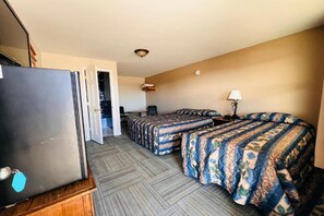 A hotel room with a bed, a desk, a chair, and a refrigerator.