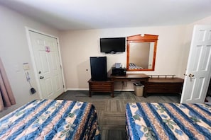 A hotel room with two beds, a television, a desk, and a mirror.
