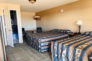A hotel room with two beds, a desk, a chair, a lamp, and a door leading to a bathroom.
