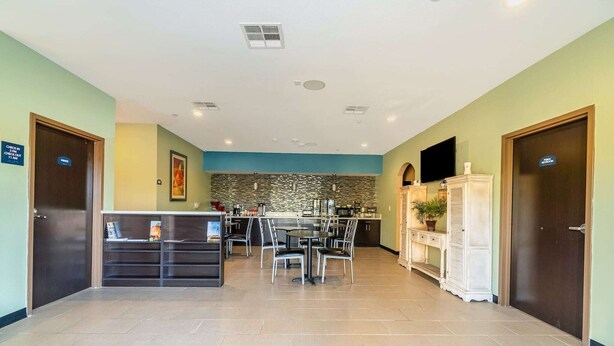 A hotel lobby with a reception desk, a dining area with chairs and tables, a kitchen in the background, and a large potted plant. - 2 Queen Beds|Non-Smoking (Moulton, TX)