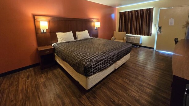 A hotel room with a large bed, two bedside tables with lamps, a chair, and a window with curtains. - King Bed|Non-Smoking (Newport News PA)