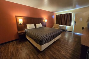 A hotel room with a large bed, two bedside tables with lamps, a chair, and a window with curtains. - King Bed|Non-Smoking (Newport News PA)
