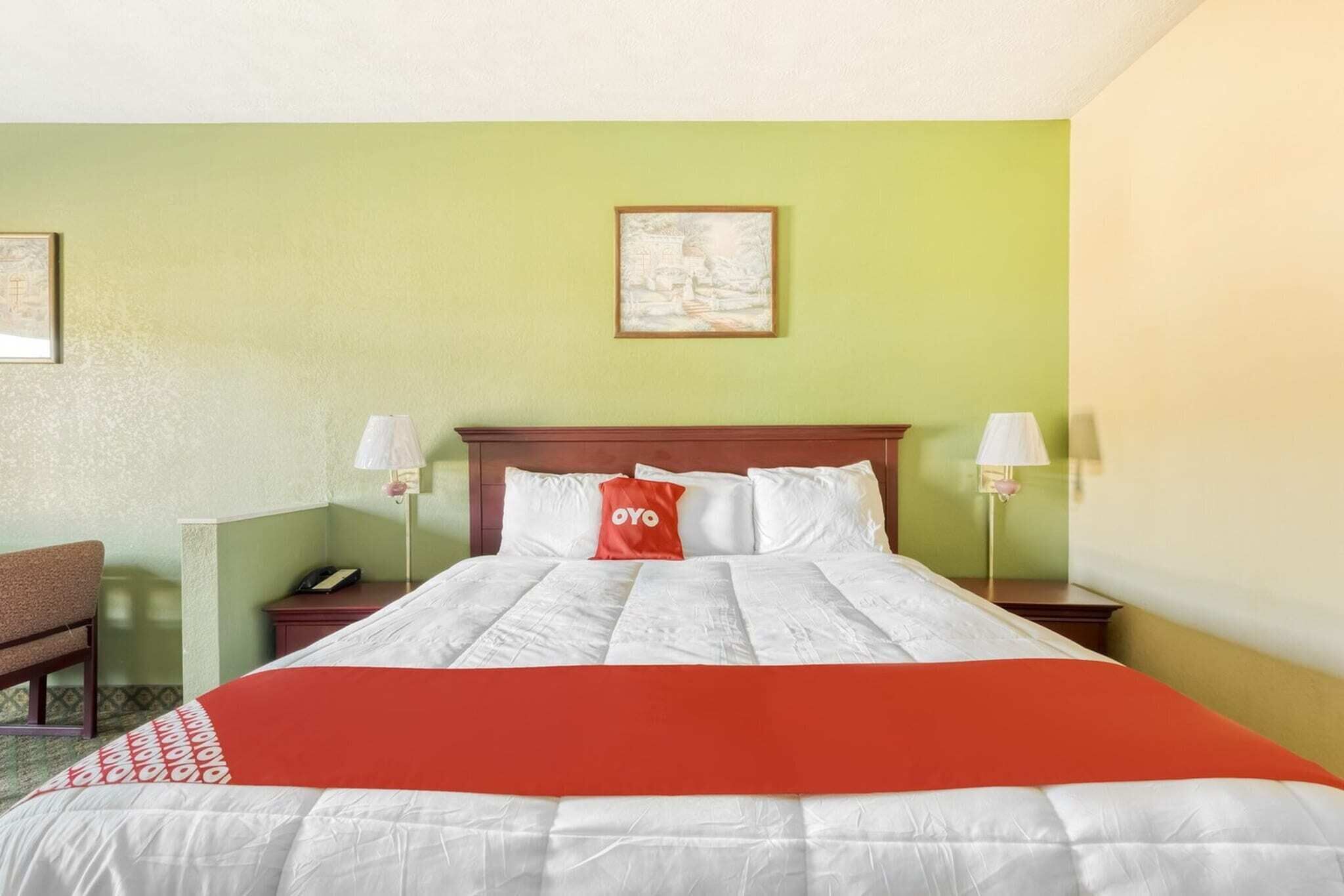 A hotel room with a bed, two bedside tables, a nightstand, a chair, and a wall-mounted picture.