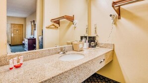 Un bagno d'albergo con lavandino, specchio, portasacchi e dispenser per asciugamani.