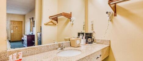 A hotel bathroom with a sink, mirror, towel rack, and a towel dispenser.