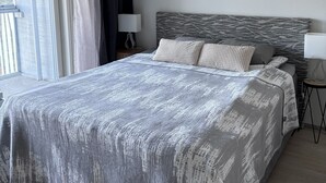 Un dormitorio moderno con una cama grande, una mesita de noche con lámpara y vistas al exterior.