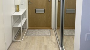 En hall med en trädörr, en vit hylla med en lampa och en mönstrad matta.