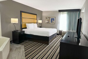 A hotel room with a bed, bedside tables, a TV, a bathroom, and a window with curtains. - Suite - King Bed|Jackson (Jackson)