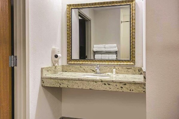 Een badkamer met een wastafel met granieten blad, een spiegel met gouden lijst en een handdoekrek met opgevouwen handdoeken.