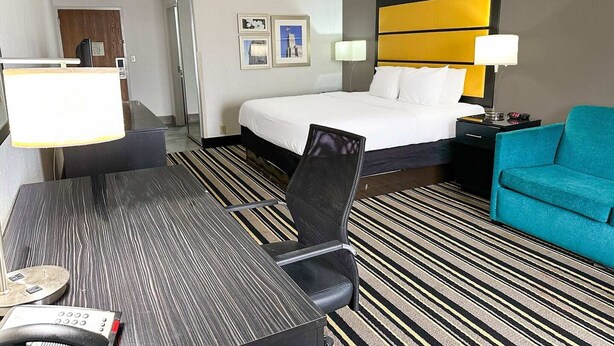 Una habitación de hotel con una cama, un escritorio con teléfono, una silla, un sofá color turquesa y una alfombra estampada.