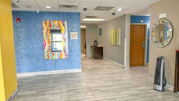 A hallway with a blue wall, a colorful artwork, a mirror, and a heater.