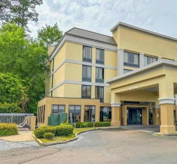 Un hotel de varios pisos con fachada amarilla, amplias ventanas y un estacionamiento.