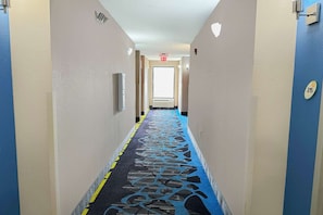 A hotel hallway with a patterned carpet, a door at the end, and a number sign on the wall. - Premium 2 Queen Bed|Jackson (Jackson)