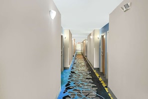 A hotel hallway with a patterned floor, doors on both sides, and light fixtures on the walls. - 2 Queen Beds Non-Smoking (Jackson)