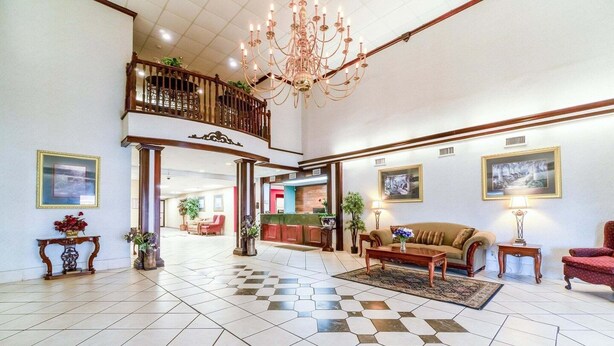 A spacious lobby with a checkered floor, a chandelier, a sofa, a red armchair, and a kitchen area in the background. - Suite - King Bed Accessible Non Smoking (Jonesboro, AR)