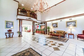 Eine geräumige Lobby mit Schachbrettboden, einer Kristallleuchtre, einem Sofa, einem roten Sessel und einem Küchenbereich im Hintergrund.