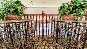A room with a patterned carpet, a wooden railing, and two potted plants on tables. - Suite - King Bed Accessible Non Smoking (Jonesboro, AR)