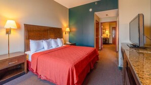 A hotel room with a bed, bedside lamps, a television, and a bathroom visible in the background. - Suite - King Bed Accessible Non Smoking (Jonesboro, AR)