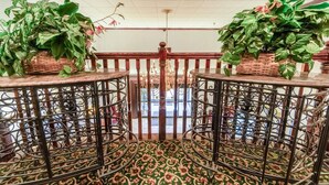 A room with a patterned carpet, a wooden railing, and two potted plants on tables. - Suite - King Bed Non - Smoking (Jonesboro, AR)