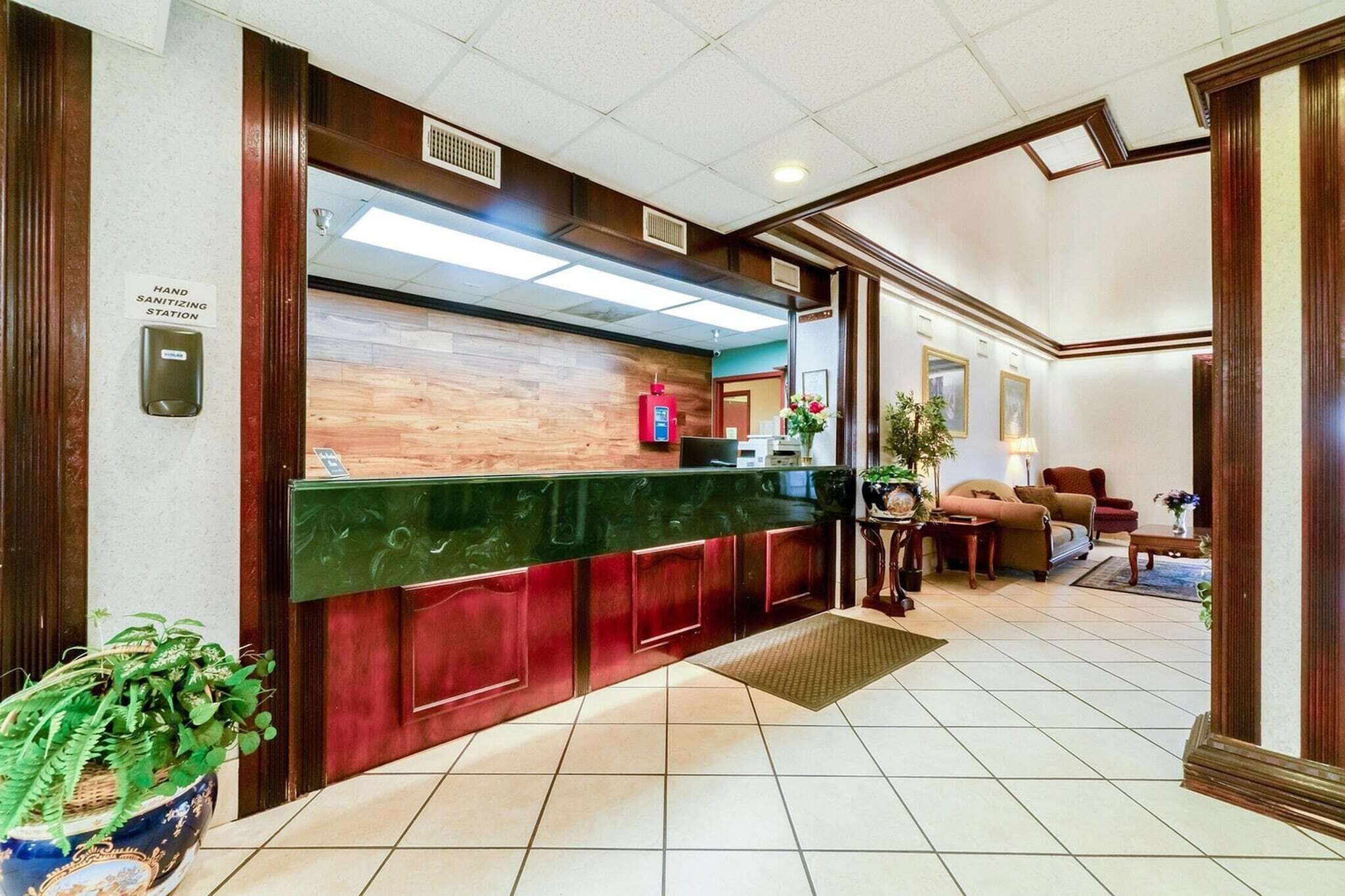 A reception area with a wooden counter, a hand sanitizing station, a fire extinguisher, and a seating area with sofas and a coffee table.