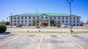 A multi-story hotel with a green roof, a central entrance, and a parking lot in front. - Suite - King Bed Non - Smoking (Jonesboro, AR)