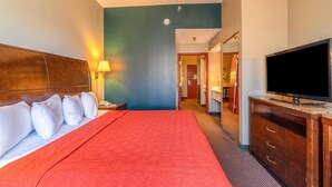 A hotel room with a bed, a TV, a desk, and a lamp. - Suite - King Bed Non - Smoking (Jonesboro, AR)
