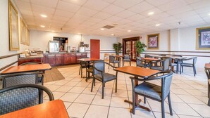 A restaurant with tiled flooring, multiple tables and chairs, a kitchen area, and framed artwork on the walls. - Suite - King Bed Non - Smoking (Jonesboro, AR)